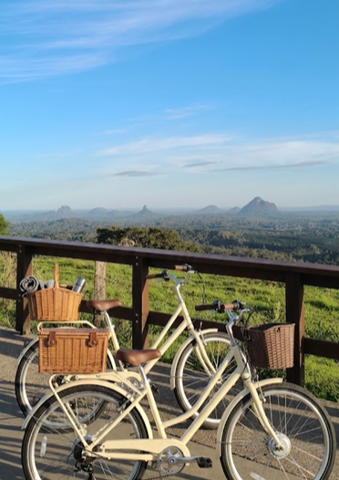 Two cream eBikes with wicker baskets parked at a Maleny lookout over the Glass House Mountains